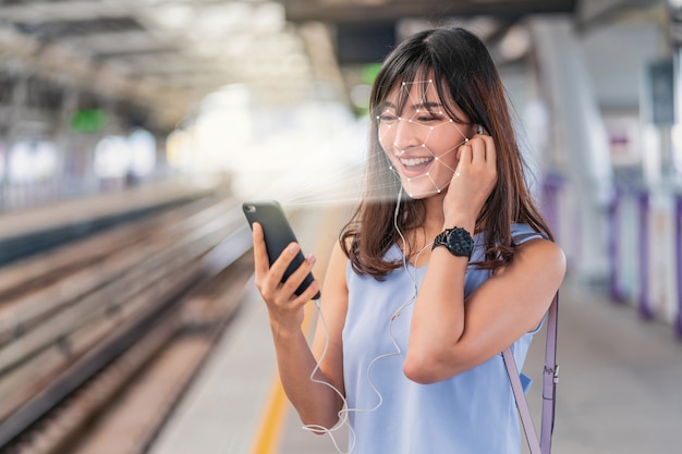 Mulher asiática usando reconhecimento de rosto via celular inteligente e ouvindo música