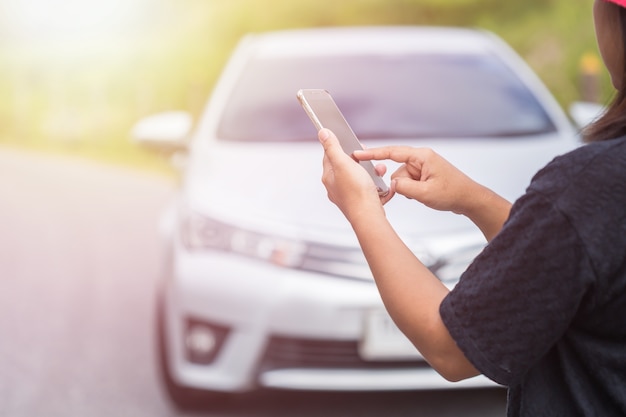 Mulher asiática usando smartphone na frente de seu carro quebrado na estrada