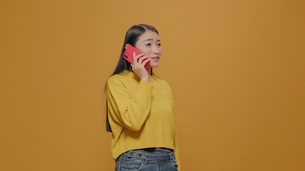 Mulher asiática usando smartphone para conversar por telefone com amigos no estúdio. Alegre adulto desfrutando de telecomunicações remotas no celular. Comunicação telefônica moderna