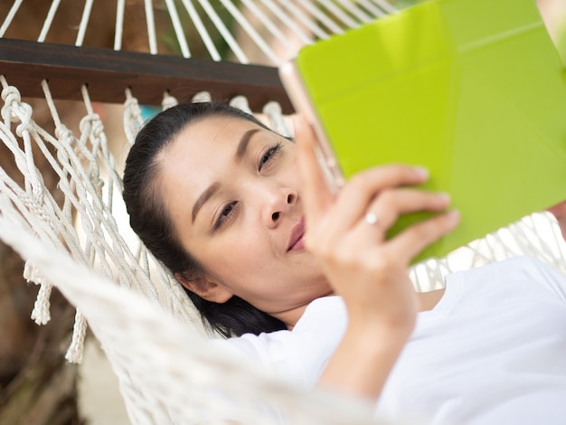 Mulher asiática usando tablet e relaxar na rede na praia na Tailândia