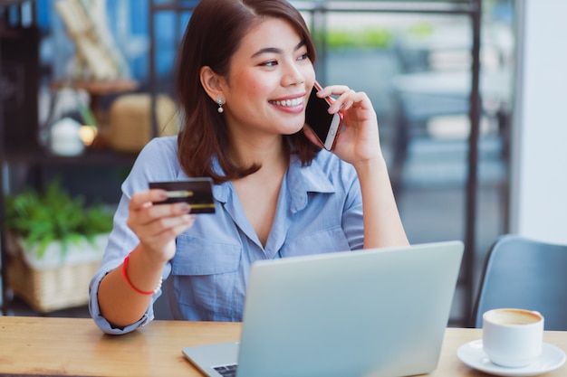 Mulher asiática, usando telefone celular com cartão de crédito e computador portátil para fazer compras de pagamento on-line na cafeteria