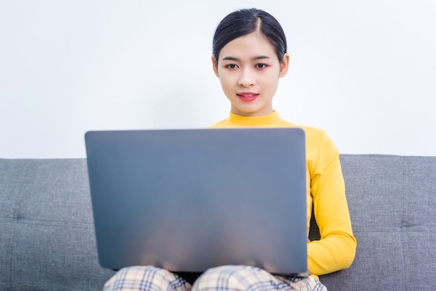 Mulher asiática usando um laptop enquanto está sentado em um sofá