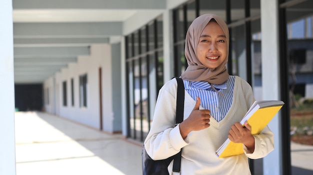 Mulher asiática vestindo hijab carregando um livro no corredor da universidade