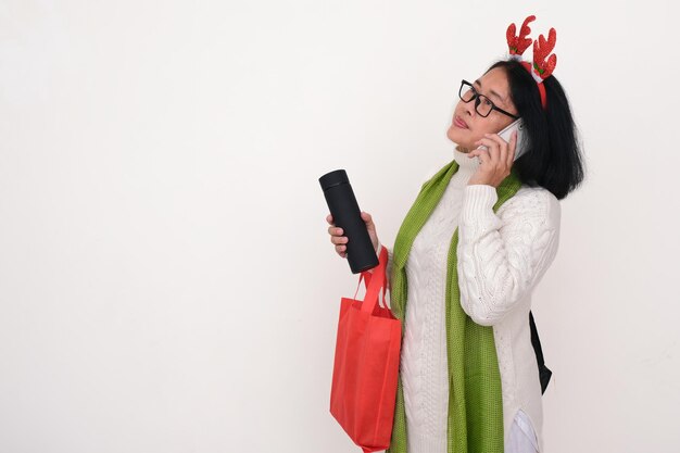 Mulher asiática vestindo roupas quentes brancas fazendo uma chamada telefônica com a mão segurando a bolsa de compras