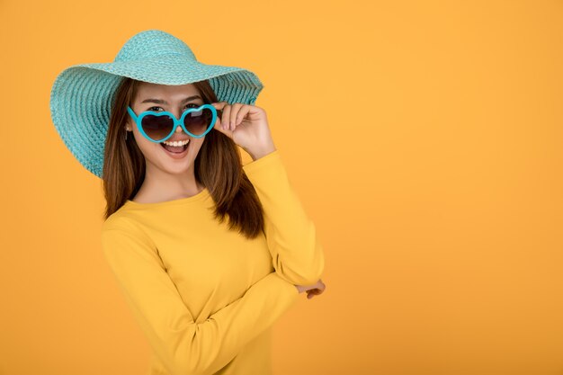 Mulher asiática vestir conceito férias com uma camisa amarela óculos de sol e chapéus são azuis e fazem rostos muito felizes.