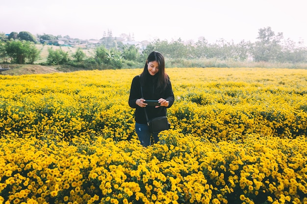 Mulher asiática viajante usando telefone celular em um campo de flores amarelas no jardim em Chiang Mai, Tailândia