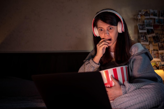 Mulher assistindo filme assustador em casa comendo fone de ouvido de pipoca