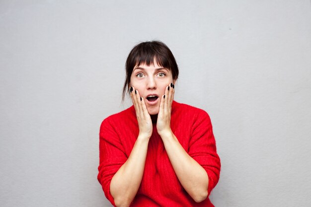 Mulher assustada com um suéter vermelho abrindo a boca em surpresa