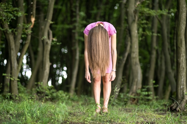 Mulher assustadora com cabelo comprido inclinado, curvada na floresta escura e temperamental.