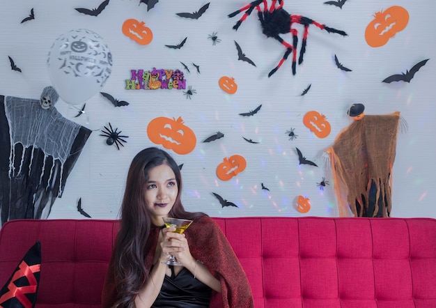Mulher atenciosa tomando uma bebida enquanto está sentada contra a decoração de Halloween na parede