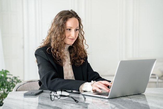 Mulher atenta trabalhando em um laptop em um ambiente sofisticado com luz natural