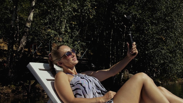 Foto mulher atirando em estabilização de gimbal de filme portátil para smartphone garota deitada no cais fazendo selfie blogger transmitindo vídeo vlogging