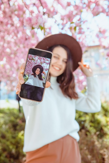 Mulher atirando em si mesma no telefone sob a árvore de sakura florescendo