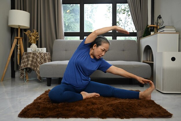 Foto mulher ativa de meia idade fazendo exercícios de alongamento na sala de estar em casa conceito de estilo de vida saudável