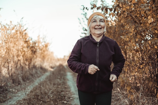 Mulher ativa e saudável com a idade de correr na floresta de outono pela manhã