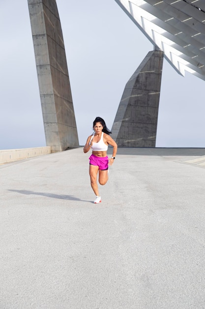 Mulher atleta em roupas esportivas correndo forte pela vista frontal da cidade
