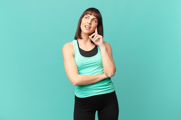 Mulher atleta sorrindo feliz e sonhando acordada ou duvidando, olhando para o lado