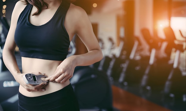 Mulher atleta usando medição de gordura corporal e tamanho da cintura com pinça digital depois de treino em ginásio de fitness estilo de vida saudável perda de peso