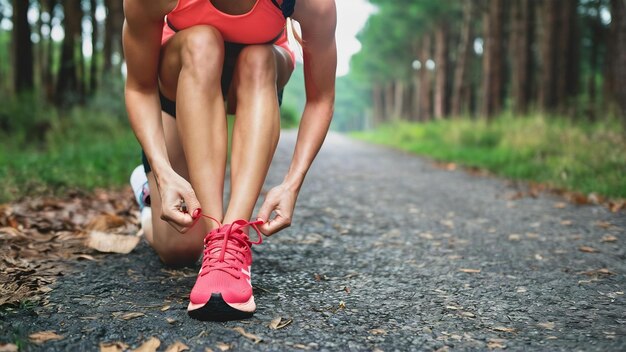 Mulher atlética caucasiana amarrando atacadores em seus sapatos de corrida cor-de-rosa antes de correr de pé na calçada