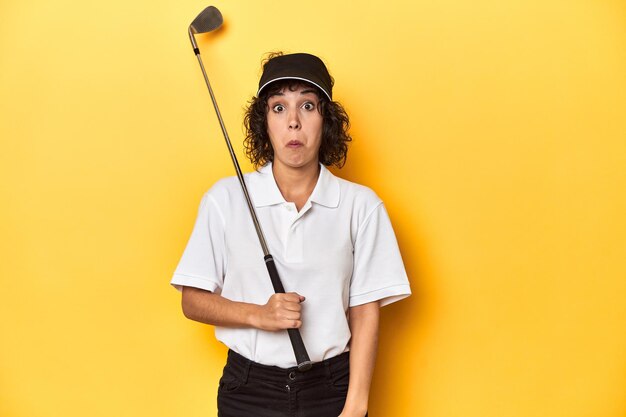 Foto mulher atlética caucasiana com cabelos encaracolados jogando golfe no estúdio encolhe os ombros e olhos abertos confusos