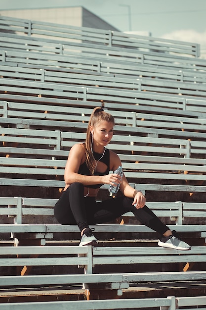 Mulher atlética em roupas esportivas e fones de ouvido ouvindo música e água potável