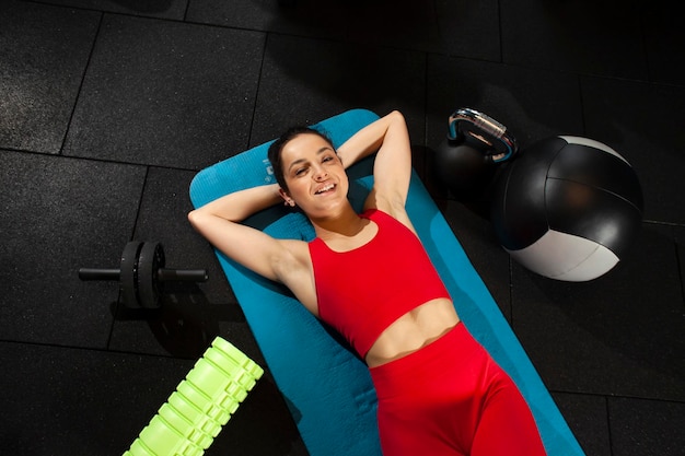 Mulher atlética em roupas esportivas vermelhas encontra-se em yoga matte no ginásio preto e sorri garota está relaxando