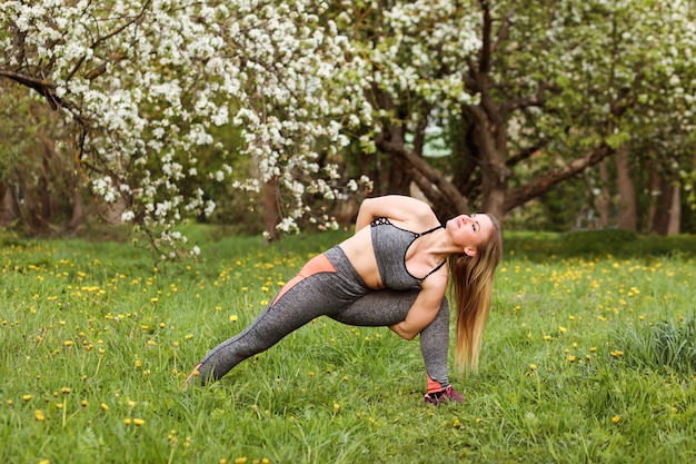 Mulher atlética fazendo exercícios de alongamento ao ar livre no parque florido