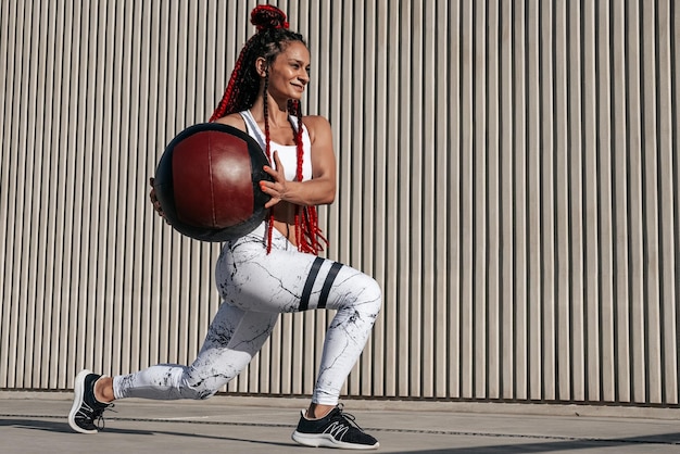 Mulher atlética fazendo exercícios de estocada com bola médica Força e motivaçãoFoto de mulher esportiva em roupas esportivas da moda