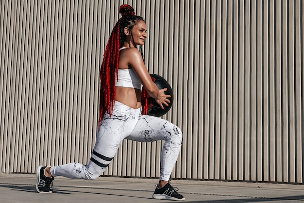 Mulher atlética fazendo exercícios de estocada com bola médica Força e motivaçãoFoto de mulher esportiva em roupas esportivas da moda