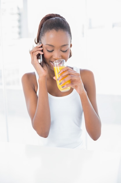 Mulher atlética feliz telefonando ao beber suco de laranja