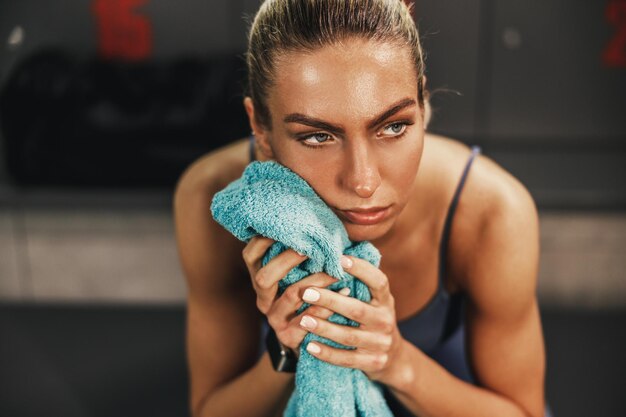 Mulher atlética pensativa se sentindo cansada e descansando no vestiário após treinamento duro.