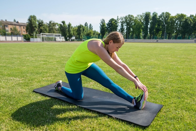 Mulher atlética praticando esportes na grama em um tapete de fitness Aquecimento de treinamento no gramado do estádio da cidade