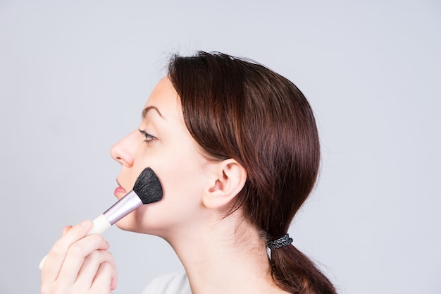 Mulher atraente aplicando blush na bochecha com uma grande escova macia de cosméticos para contornar e colorir o rosto