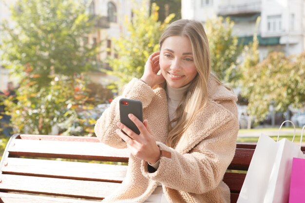 Mulher atraente arrumando o cabelo enquanto tira selfies com seu smartphone no parque em um dia quente e ensolarado de outono.