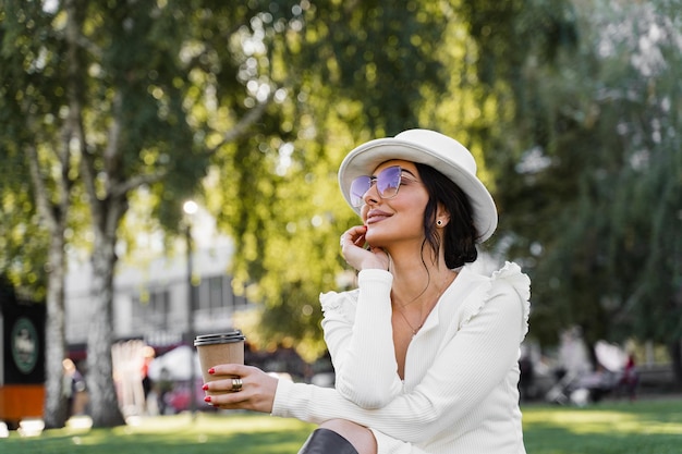 Mulher atraente com café na grama. Modelo usava estilo oficial branco desfrutar de café.