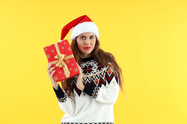 Mulher atraente com chapéu de Papai Noel segurando uma caixa de presente em fundo amarelo