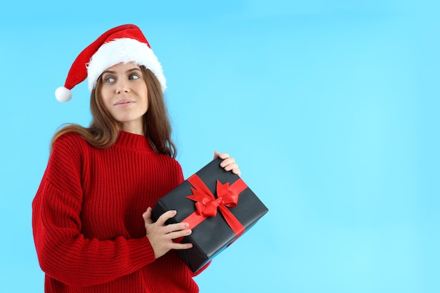 Mulher atraente com chapéu de Papai Noel segurando uma caixa de presente no fundo azul