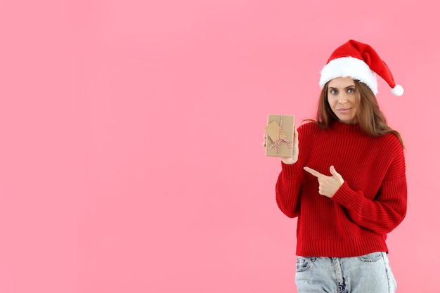 Mulher atraente com chapéu de Papai Noel segurando uma caixa de presente no fundo rosa