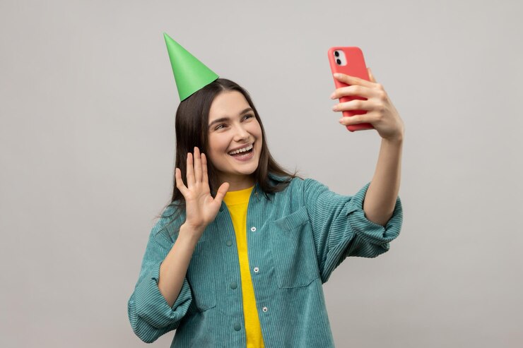 Foto mulher atraente com cone de festa fazendo selfie ou transmitindo transmissão ao vivo acenando com a mão dizendo olá