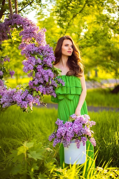 mulher atraente com vestido verde posando perto de decoração de flor lilás.