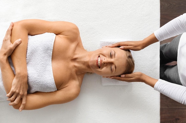 Foto mulher atraente de meia-idade a receber uma massagem relaxante na cabeça num salão de spa de luxo.
