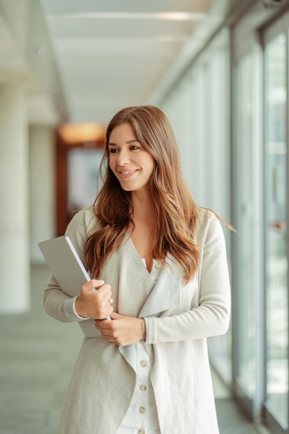 Mulher atraente e bonita segurando laptop trabalhando em um escritório moderno olhando para longe