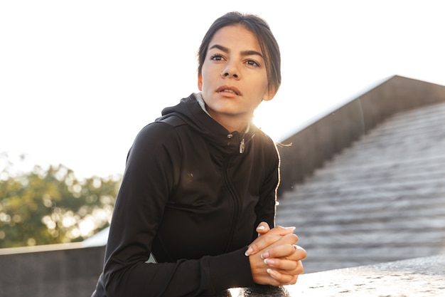 Mulher atraente e confiante em fitness vestindo roupas esportivas, fazendo exercícios ao ar livre, posando