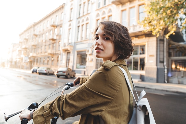 Mulher atraente e elegante de casaco andando de bicicleta em uma rua da cidade