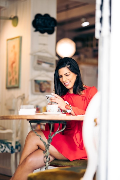 Mulher atraente e feminina olha para o celular e bebe um café