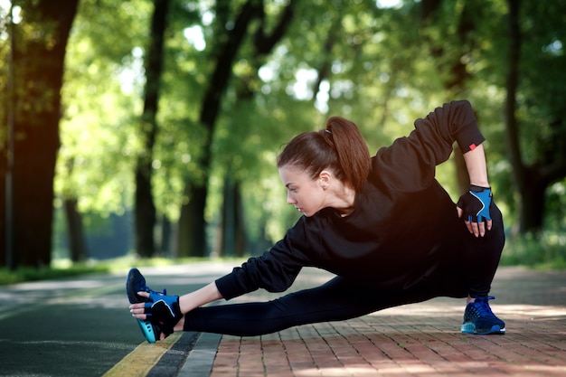 Mulher atraente e forte, estendendo-se antes da aptidão no parque de verão. Conceito de esportes. Estilo de vida saudável