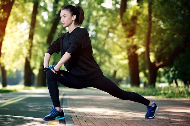 Mulher atraente e forte, estendendo-se antes da aptidão no parque de verão. Conceito de esportes. Estilo de vida saudável