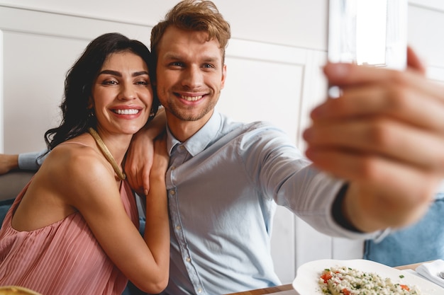 Mulher atraente encostada no ombro do cavalheiro enquanto um homem tira uma foto com o smartphone