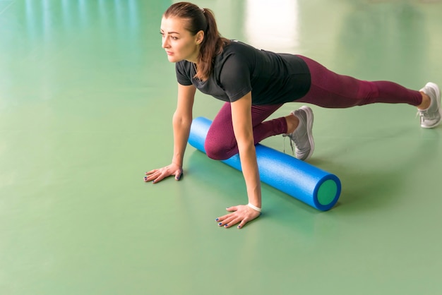 Mulher atraente, exercitar a aptidão de pilates, fazendo exercícios de rolo de espuma e posando no moderno centro de fitness brilhante