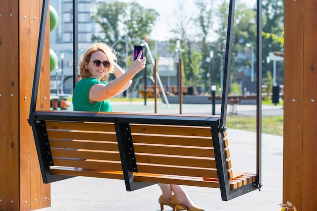 mulher atraente feliz em óculos de sol tirando foto de selfie no telefone conversando com assinantes de amigos